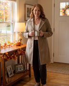 Lady Luxe velvet-lined coat worn by a mature model in a cozy autumn-decorated home entryway